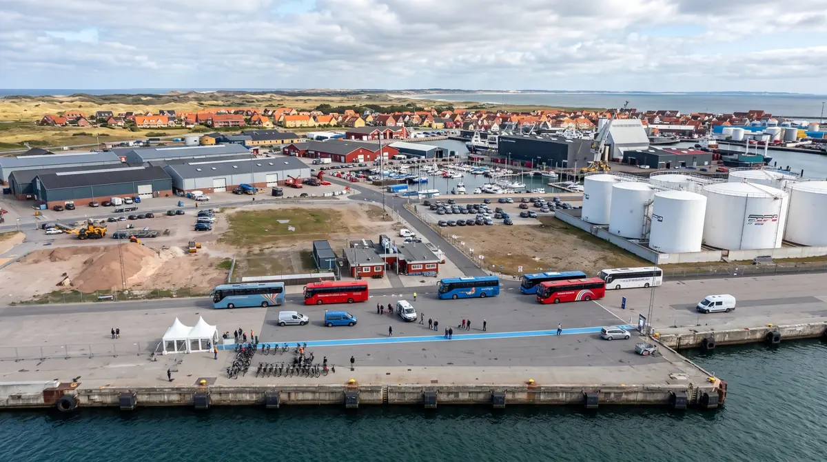 Skagen Kreuzfahrt-Pier im Hafen von Skagen mit Shuttlebussen, Leihfahrrädern und blauer Fußgängerlinie, dahinter der Ort mit roten Dächern und Dünen